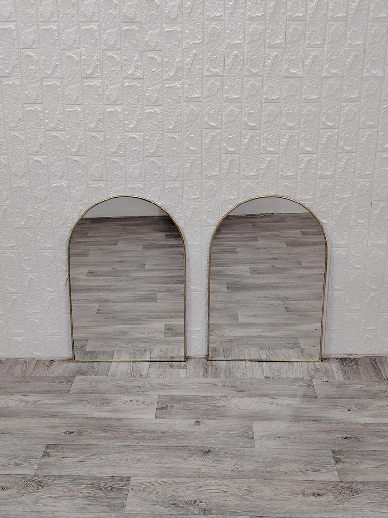 Op de afbeelding: Twee gouden boogspiegels met een houten vloer erachter.