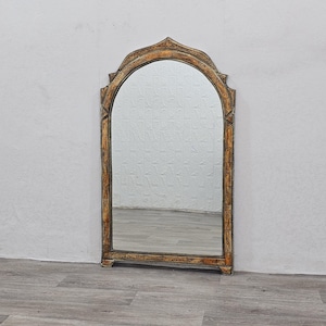 May include: A tall, arched mirror with a gold and brown ornate frame. The frame has intricate carvings and a distressed finish.