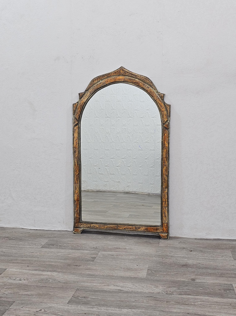 May include: A tall, arched mirror with a gold and brown ornate frame. The frame has intricate carvings and a distressed finish.