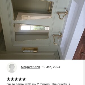 May include: Two gold-framed, beveled-edge mirrors with a decorative design, mounted on a light green wall. The mirrors are angled and reflect the surrounding space.
