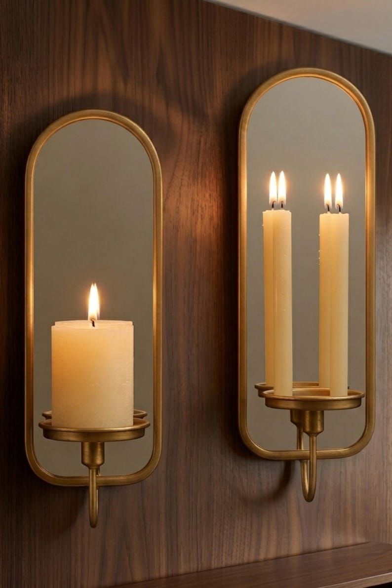 Puede incluir: Dos apliques de pared con marco dorado, espejos y velas encendidas. Uno tiene una vela de pilar gruesa, el otro dos velas delgadas. Los apliques est&aacute;n montados en una pared de paneles de madera oscura, creando un ambiente c&aacute;lido.