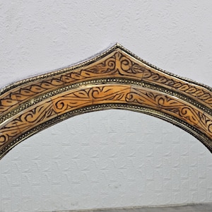 May include: A decorative arched mirror frame with intricate carvings and a gold finish. The frame is made of wood and has a unique design.