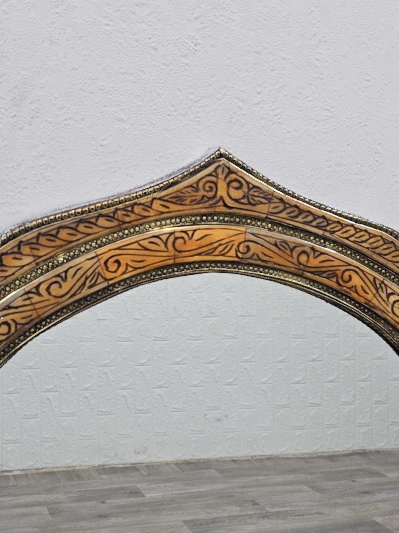 May include: A decorative arched mirror frame with intricate carvings and a gold finish. The frame is made of wood and has a unique design.