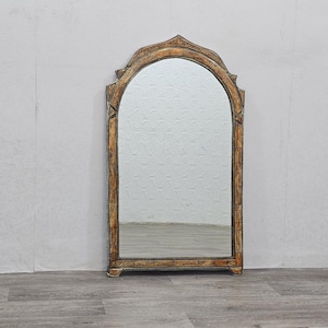May include: A tall, arched mirror with a decorative, ornate frame. The frame is painted in a gold and brown color scheme with intricate floral designs.