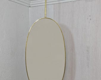 May include: An oval mirror suspended from the ceiling with a brass rod. The mirror features a brass frame and a light-colored reflective surface. The design is simple and elegant, suitable for various interior styles.