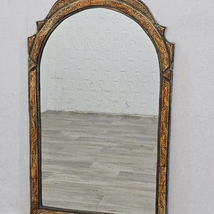 May include: A large, arched mirror with a decorative, ornate frame. The frame is made of wood and is painted in a light brown color. The frame has a carved design with intricate details.