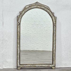 May include: A large, arched mirror with an ornate, silver-painted frame. The frame has a detailed, carved design with a distressed finish.