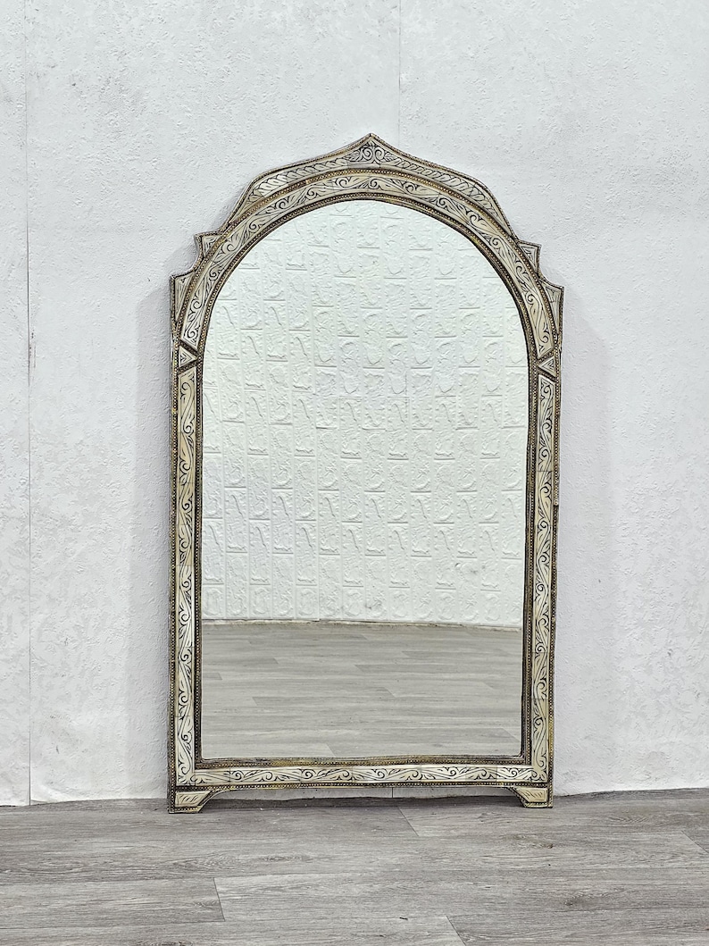 May include: A large, arched mirror with an ornate, silver-painted frame. The frame has a detailed, carved design with a distressed finish.