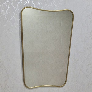 May include: A gold-framed wall mirror with a wavy, asymmetrical shape. The mirror has a simple, modern design.