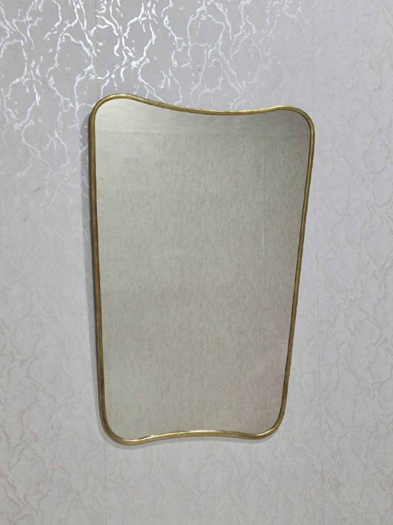 May include: A gold-framed wall mirror with a wavy, asymmetrical shape. The mirror has a simple, modern design.