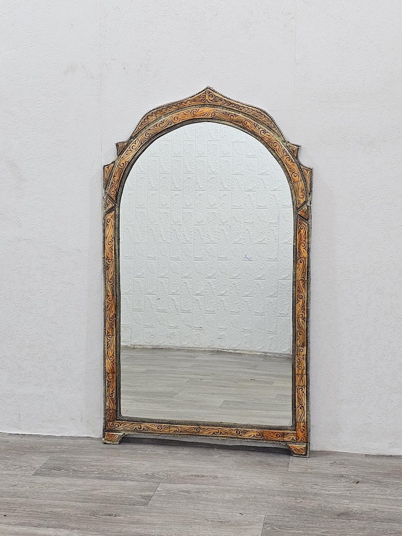 May include: A large, ornate mirror with a gold-painted frame. The frame has a carved design with a brown and gold finish. The mirror is arched at the top and has a rectangular shape.