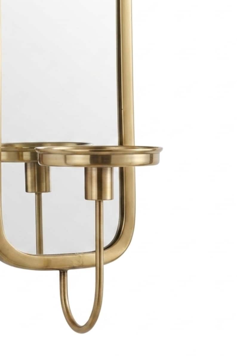 Puede incluir: Aplique de pared dorado con espejo y candelero. El espejo es rectangular con bordes redondeados. El candelero es circular y la base es curva. El dise&ntilde;o es simple y elegante.