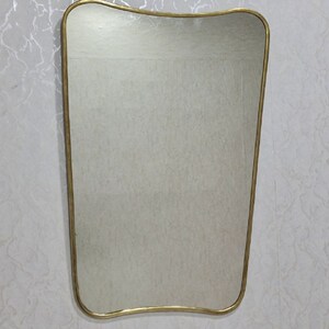 May include: A gold-framed mirror with a wavy, asymmetrical shape. The mirror is rectangular and has a smooth, reflective surface.