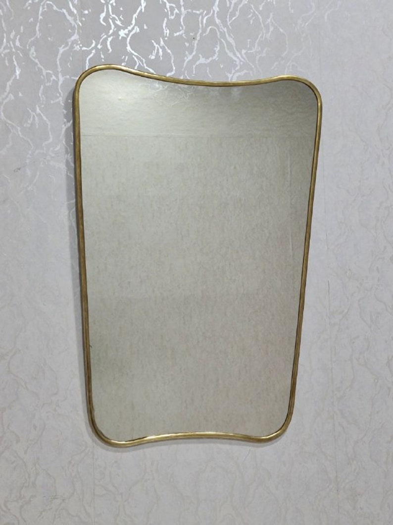 May include: A gold-framed mirror with a wavy, asymmetrical shape. The mirror is rectangular and has a smooth, reflective surface.