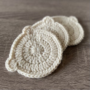 May include: Three crocheted beige coasters with a scalloped edge. The coasters are stacked on top of each other.