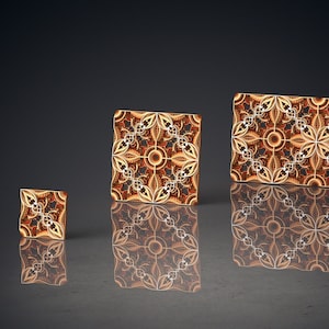 May include: Three decorative tiles with intricate geometric patterns in shades of brown and gold. The tiles are arranged in a row from smallest to largest.