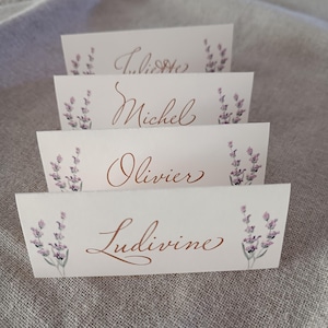 Peut inclure: Quatre cartons de table blancs avec des noms en écriture brune élégante : Juliette, Michel, Olivier et Ludivine. Chaque carton présente une illustration de brin de lavande en violet et vert, pour mariages ou événements.