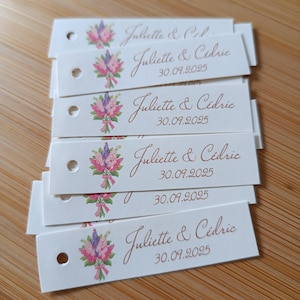 Peut inclure: Plusieurs étiquettes rectangulaires blanches avec un motif floral et le texte "Juliette & Cédric" et "30.09.2025" imprimé en marron. Chaque étiquette a un petit trou en haut.