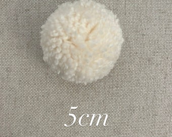 May include: A white pom pom, 5 cm in diameter, against a beige fabric background.