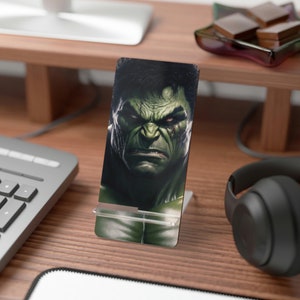 Könnte beinhalten: Ein Handyständer mit einem grünen und schwarzen Bild von Hulk, einem fiktiven Superhelden. Der Ständer ist aus klarem Kunststoff und hat eine Metallbasis.