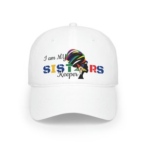 Puede incluir: Gorra de béisbol blanca con el texto "I am My Sisters Keeper" y una silueta negra de una mujer con un turbante de colores y una estrella de cinco puntas.