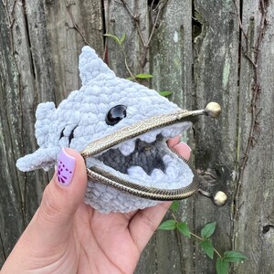 May include: A gray crocheted shark coin purse with a metal clasp. The purse is open and the inside is visible.