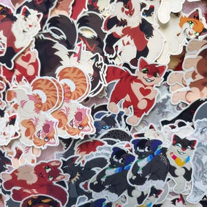 Op de afbeelding: Een verzameling kleurrijke kattenstickers in verschillende poses en ontwerpen. De stickers tonen katten met verschillende vachtpatronen, waaronder calico, tabby en effen kleuren. Sommige katten hebben hartvormige markeringen. Geschikt voor het decoreren van laptops, waterflessen of notitieboekjes.