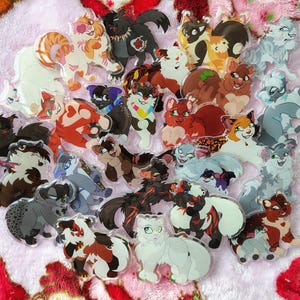 Op de afbeelding: Een verzameling kleurrijke acryl bedels met katten als thema. De bedels tonen verschillende kattenontwerpen in verschillende kleuren en patronen, waaronder oranje, wit, zwart en grijs. Elke bedel heeft een unieke kattenillustratie.