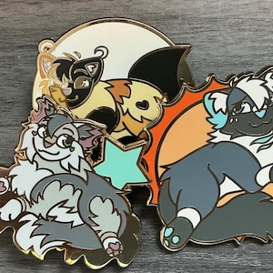 Op de afbeelding: Set van vier emaillepins met cartoon dierenfiguren. De pins zijn goudkleurig met kleurrijke details. Eén pin heeft een zwart-witte kat met een roze neus, een andere heeft een grijs-witte kat met een roze neus, een andere heeft een zwart-witte kat met een blauwe neus en de laatste pin heeft een zwart-witte kat met een blauwe neus.