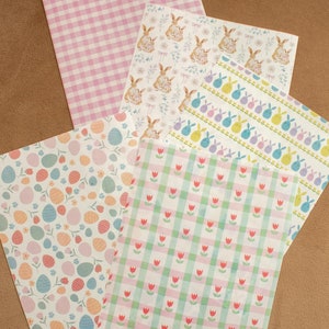 Pode incluir: Quatro folhas de papel decorativo com diferentes padrões temáticos de Páscoa. Os padrões incluem vichy rosa e branco, coelhos com flores, ovos com flores e vichy verde e rosa com tulipas.