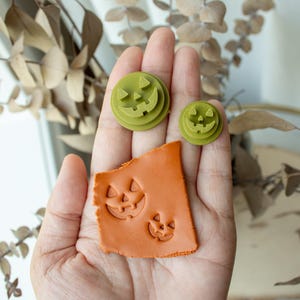 Puede incluir: Cortadores de galletas y arcilla estampada con temática de Halloween, verdes y naranjas. Los cortadores verdes son redondos con una cara de jack-o'-lantern tallada. La arcilla naranja tiene caras de jack-o'-lantern estampadas.