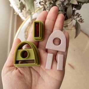 May include: A set of four cookie cutters in green and pink. The cutters are shaped like an archway, a rectangle, and two small rectangles. The archway cutter has a small circle cut out of the center.