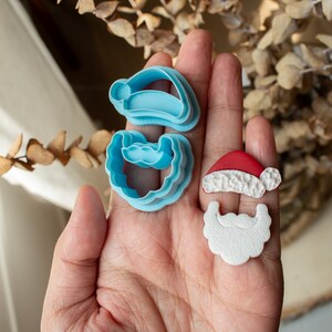 May include: A set of blue plastic cookie cutters shaped like a Santa hat and beard, and a white fondant Santa hat and beard.