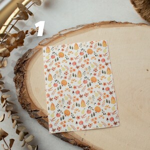 May include: A sheet of white paper with a repeating pattern of small orange pumpkins, green leaves, red apples, and yellow pears. The pattern is surrounded by a white border.