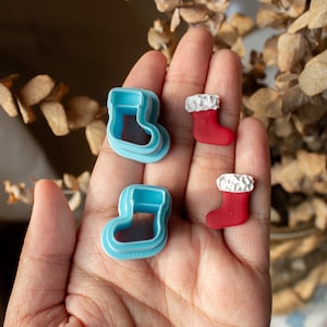 Puede incluir: Dos cortadores de galletas de medias de Navidad de plástico azul y dos adornos de medias de Navidad rojos y blancos.