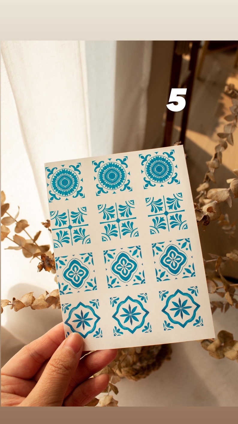 May include: A sheet of 9 blue and white patterned tile stickers. The stickers are arranged in 3 rows of 3. The stickers are on a white background.