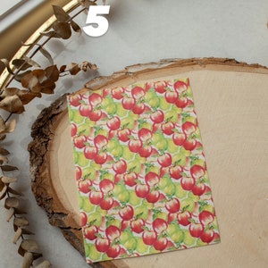 May include: A sheet of paper with a repeating pattern of red apples and green pears. The paper is on a wooden surface.