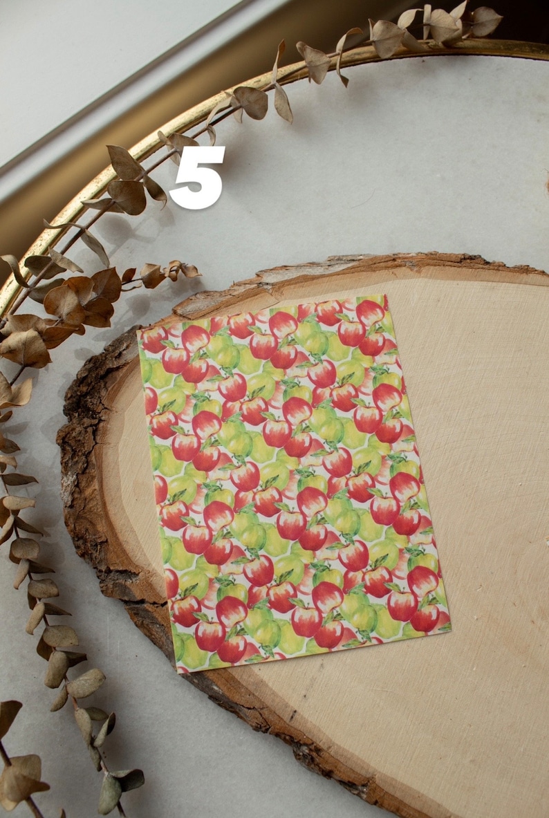 May include: A sheet of paper with a repeating pattern of red apples and green pears. The paper is on a wooden surface.