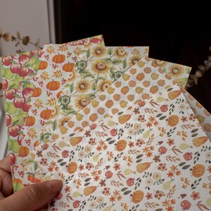 May include: Four sheets of decorative paper with autumnal themes. The papers feature different patterns including pumpkins, sunflowers, pears, apples, and leaves in shades of orange, yellow, brown, and red.