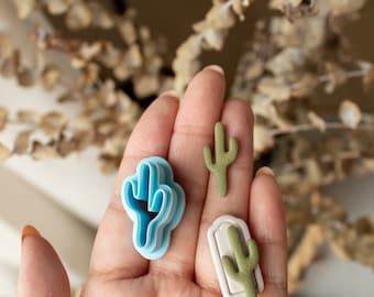 Peut inclure: Trois emportes-pièces en forme de cactus, un bleu, un blanc avec un cactus vert et un cactus vert. Les emportes-pièces sont sur une main.