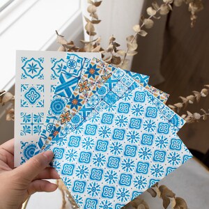 May include: Set of four blue and white patterned paper sheets with geometric designs. The sheets are folded and held in a hand.