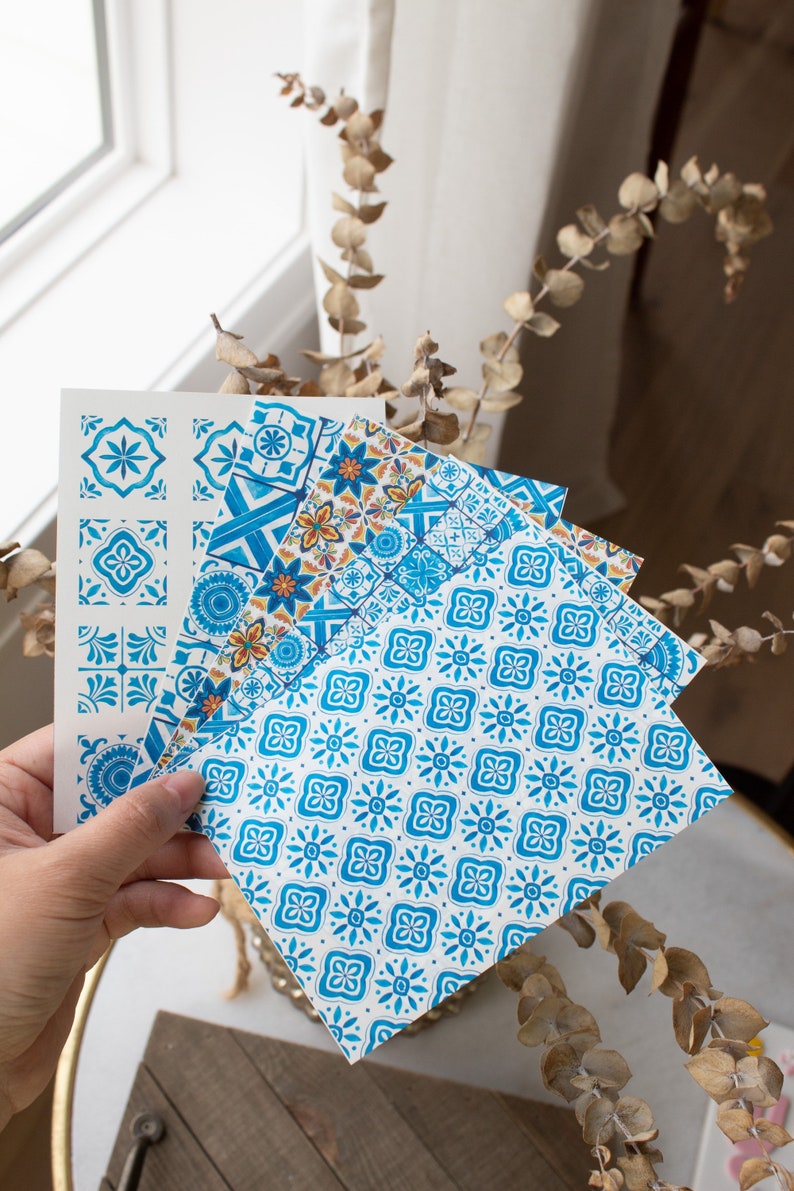 May include: Set of four blue and white patterned paper sheets with geometric designs. The sheets are folded and held in a hand.
