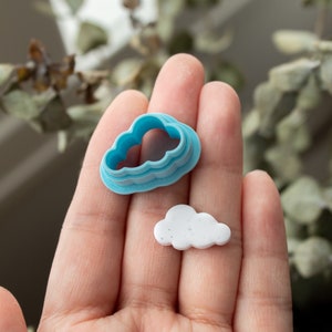 May include: A blue plastic cloud-shaped cookie cutter and a white cloud-shaped cookie. The cookie cutter has a double layer.