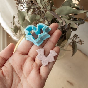 May include: Two blue plastic cookie cutters in the shape of a flower. One cutter is stacked on top of the other. A pink flower-shaped cookie is next to the cutters.