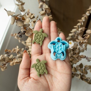May include: Three turtle-shaped cookie cutters, two green and one blue. The green cutters are made of a textured material, while the blue cutter is smooth plastic.