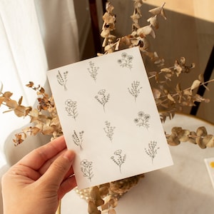 May include: A sheet of white paper with 12 black and white floral illustrations. The illustrations are of different types of flowers and leaves.