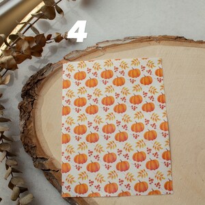 May include: A sheet of white paper with a repeating pattern of orange pumpkins, red berries, and yellow leaves. The paper is on a wooden surface.