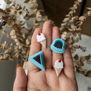 May include: A set of four blue plastic cookie cutters in the shape of an ice cream cone, a triangle, and two different sizes of a half circle. The ice cream cones have a red cherry on top.