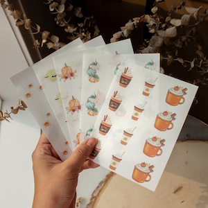 Puede incluir: Un conjunto de cinco hojas de pegatinas transparentes con diseños de otoño. Las pegatinas incluyen calabazas, arañas y una taza de café con crema batida y el texto "Pumpkin Spice".