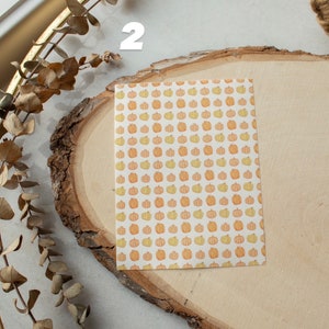 May include: A white card with a pattern of orange and yellow pumpkins on a wooden surface. The number "2" is written on the surface.